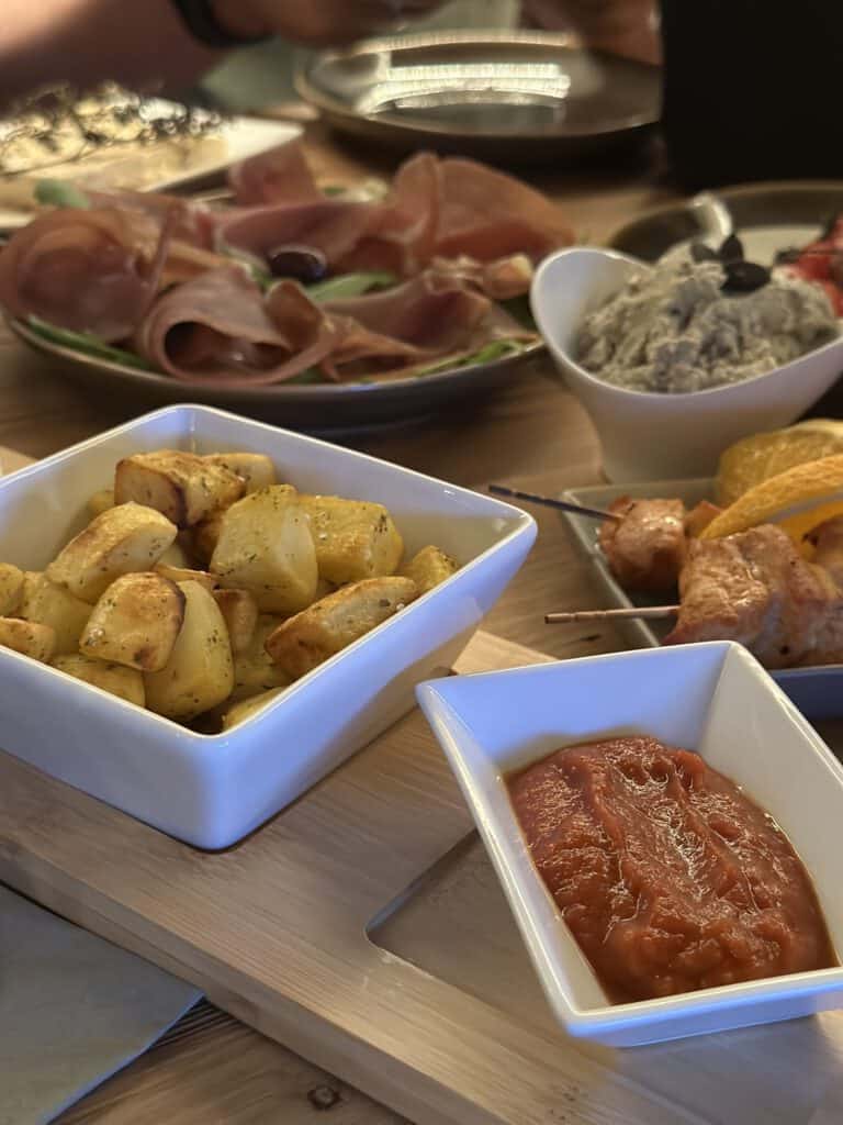 Verschiedene Aufschnitte, Kartoffeln, Tomatensauce und Dips auf einem Holzbrett.